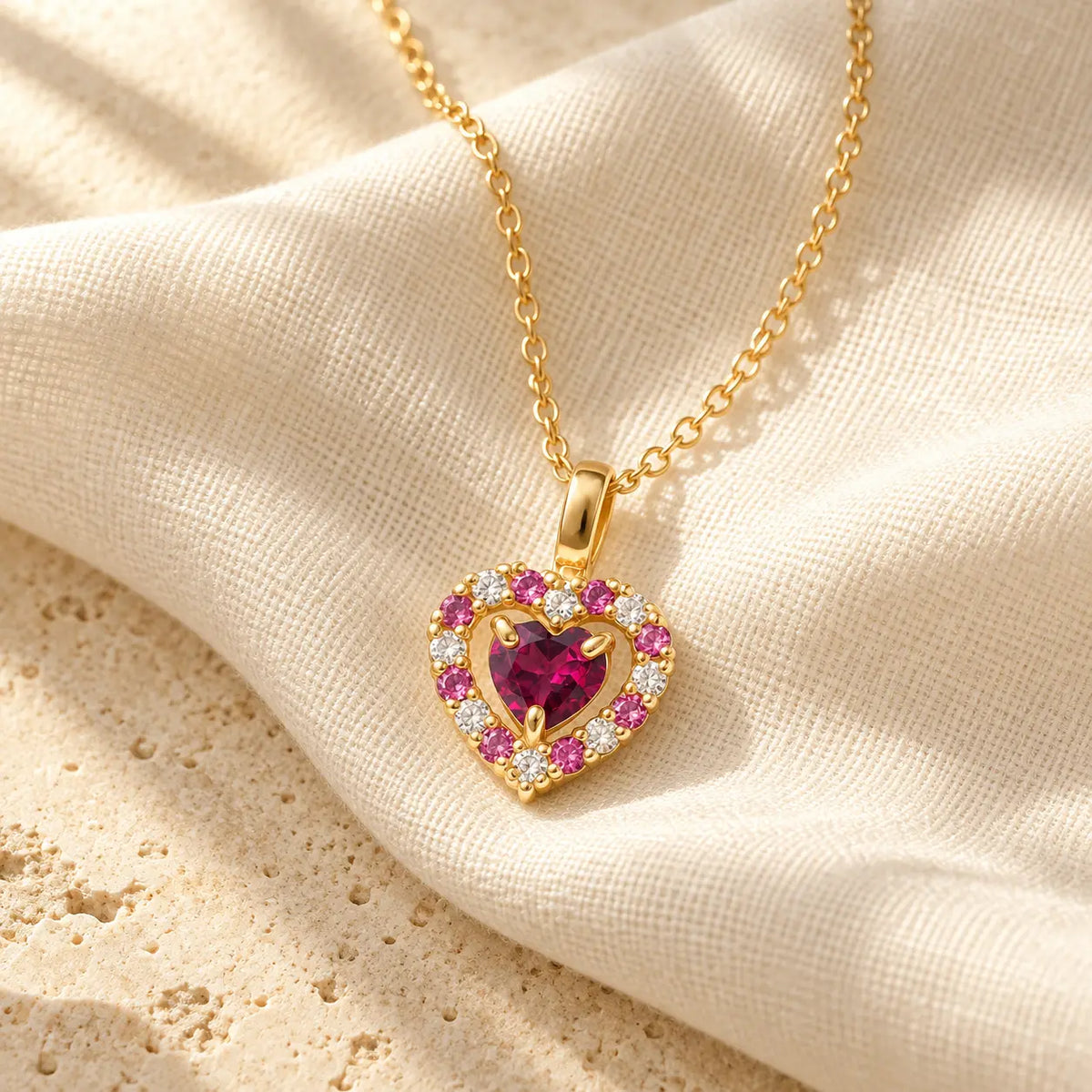 Rhodolite garnet heart pendant necklace in gold vermeil resting on ivory linen in warm natural light.