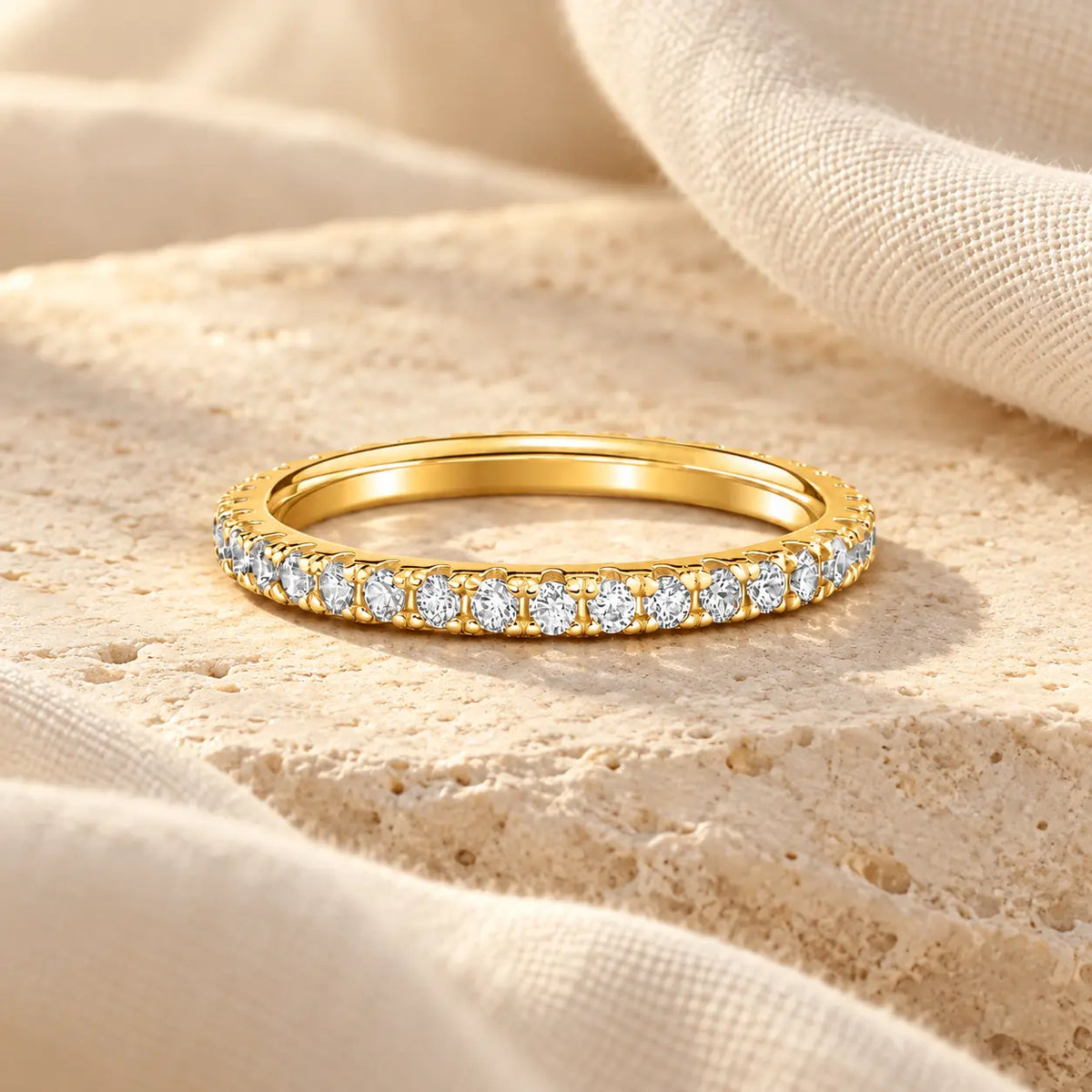 Gold vermeil eternity ring with clear simulated diamonds resting on pale limestone beside ivory linen.