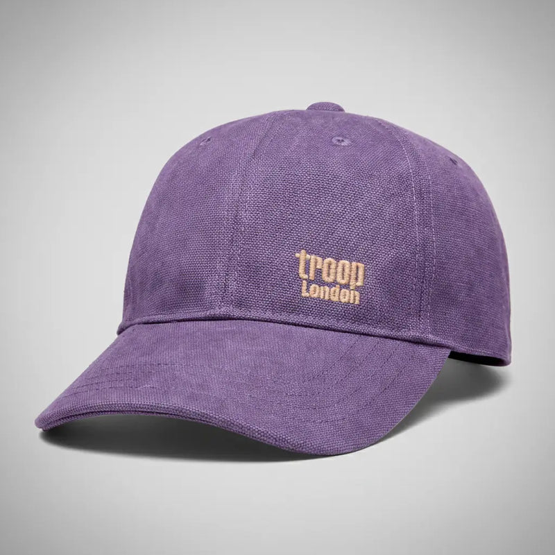 Troop London stone-washed canvas baseball cap in purple with gold embroidered logo, angled three-quarter view on a silver backdrop