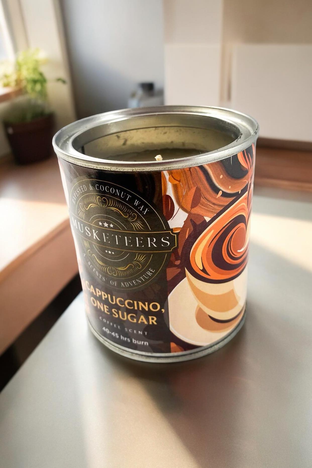 Musketeers coffee candle labeled Cappuccino with 1 sugar, featuring a realistic coffee cup design and warm, inviting tones.