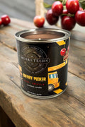 Cherry Amaretto Candle by Musketeers featuring a glass jar with a lit wick and cherry-themed design.