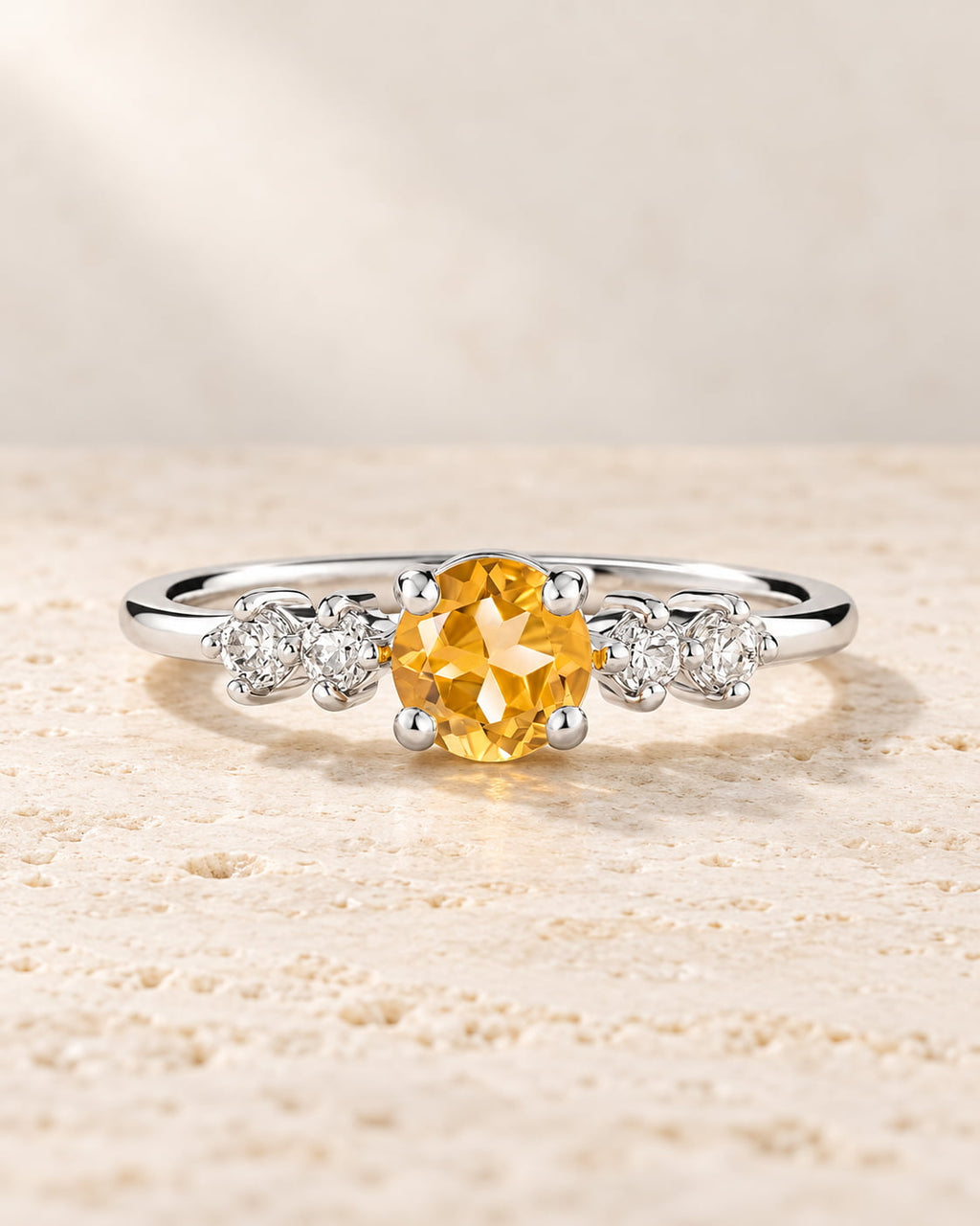 Sterling silver ring with a golden citrine centre stone and four clear accent stones on pale travertine.