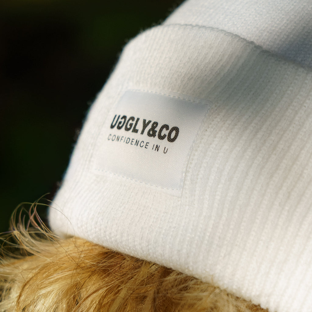 Close-up of white Uggly and Co beanie with visible logo detail, showing soft knit fabric and snug fit.