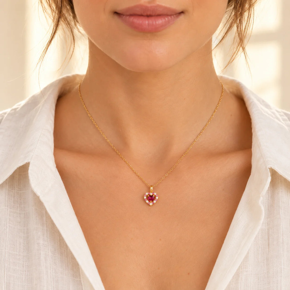 Woman wearing a delicate red heart rhodolite garnet pendant necklace in 18k gold vermeil with a cream linen blouse.