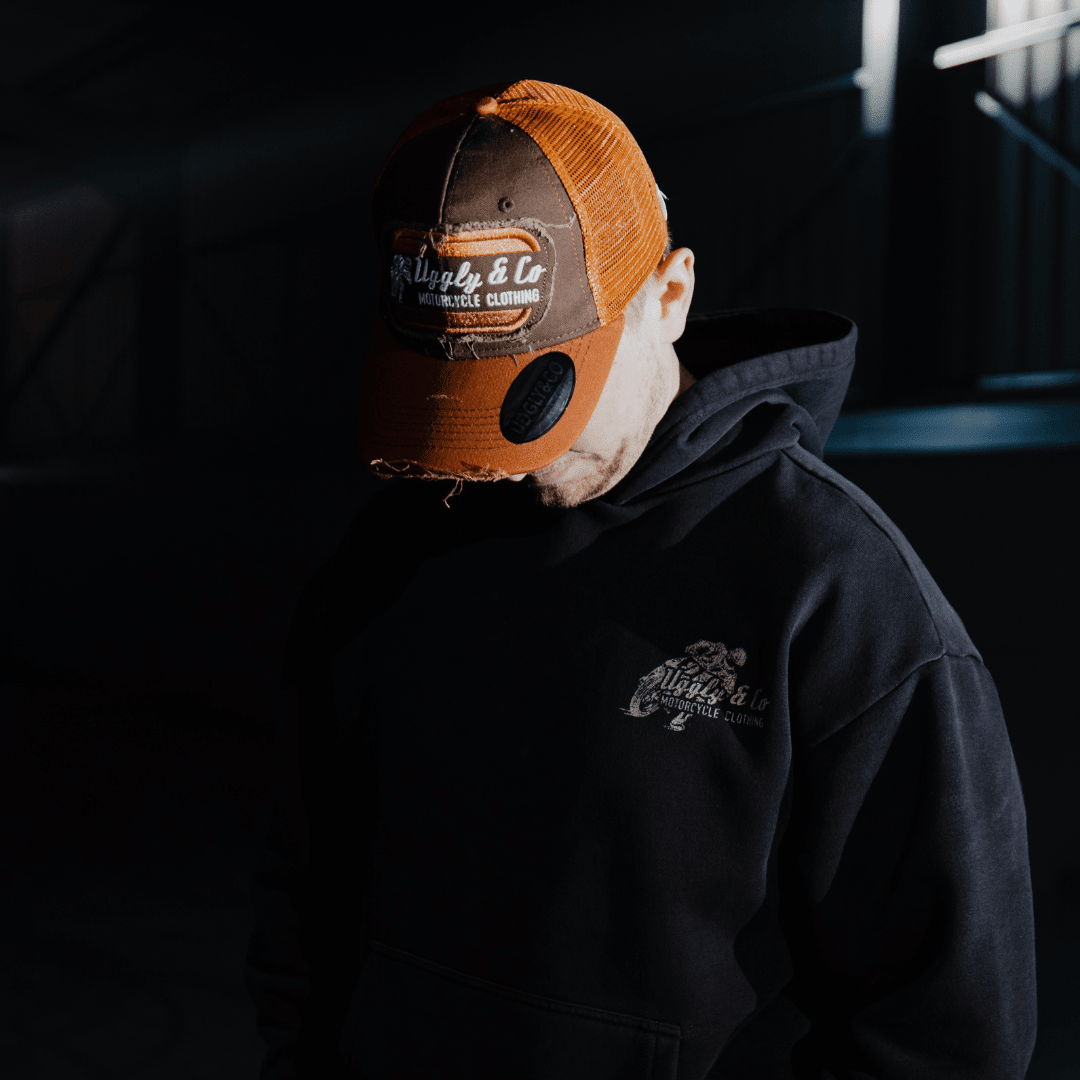 Rust-colored Uggly and Co flat track trucker hat with mesh back and curved brim.