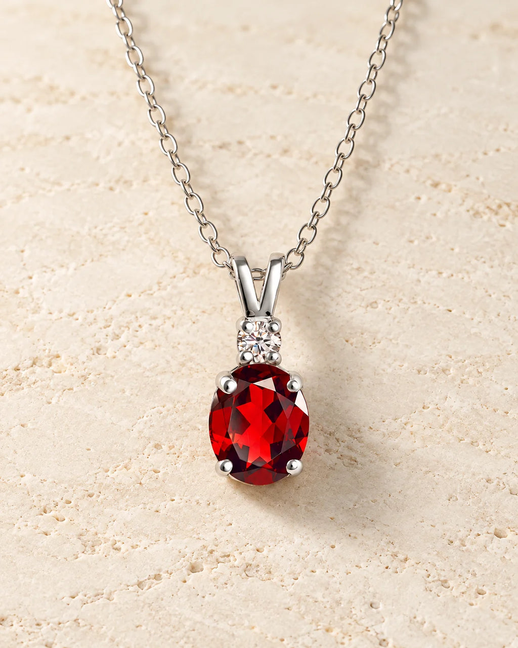 Sterling silver garnet pendant necklace on ivory travertine background, showcasing a Vianne Jewellery elegant gemstone pendant.