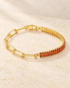 Gold plated bracelet with paperclip links and orange-red baguette stones arranged on pale travertine.