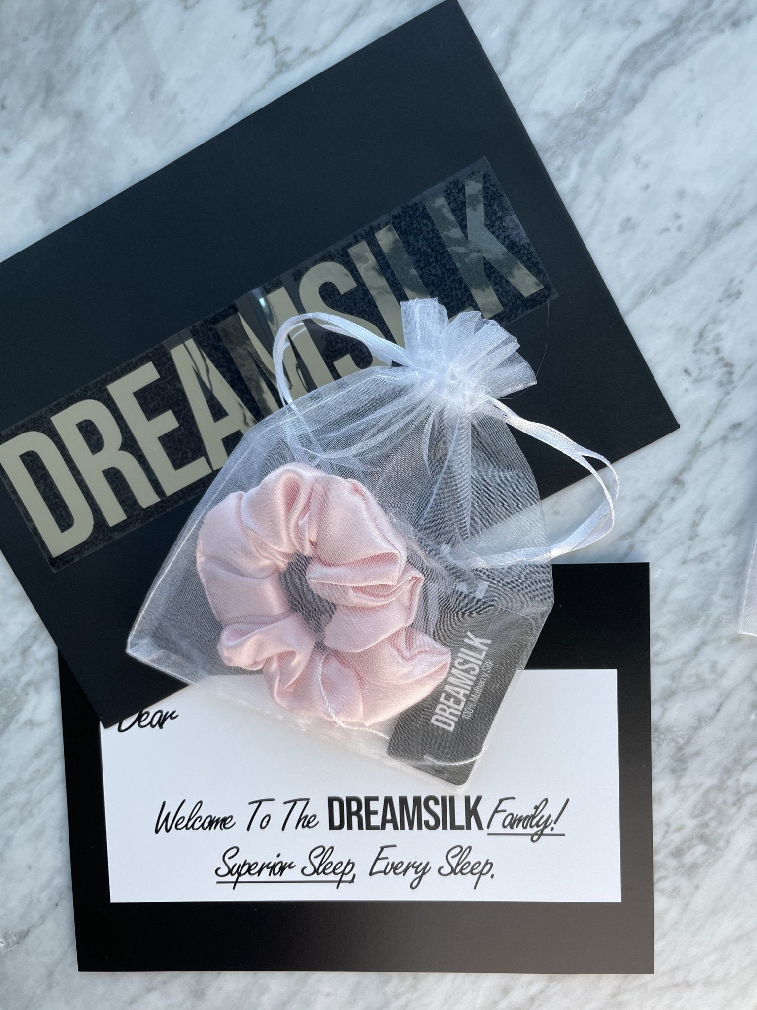 Pink silk scrunchie from DREAMSILK, a soft and shiny hair accessory with a smooth, luxurious fabric appearance.