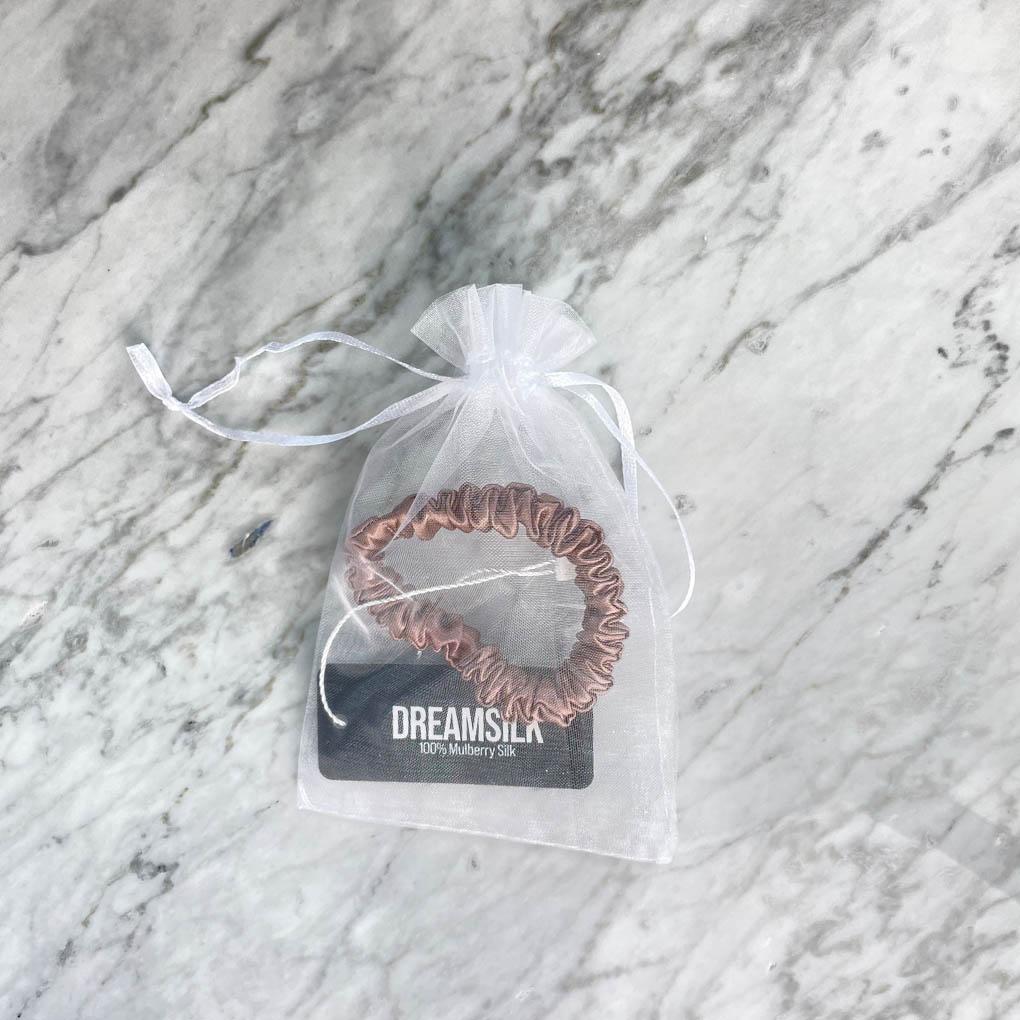 Bronze silk scrunchie by DREAMSILK, skinny style, shown coiled with smooth, shiny silk fabric on a neutral background.