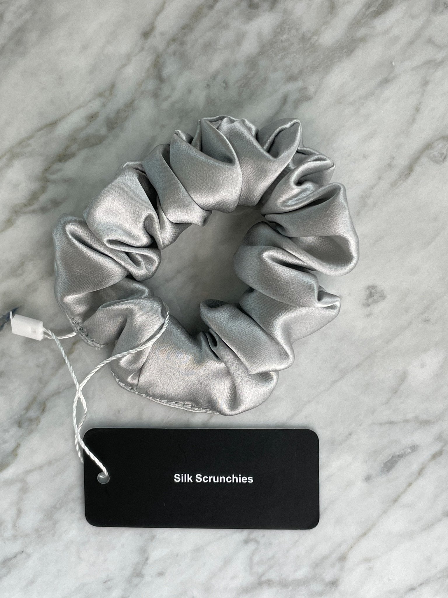 Silver silk scrunchie from DREAMSILK, showcasing a smooth, shiny fabric with a gentle, rounded shape on a plain background.