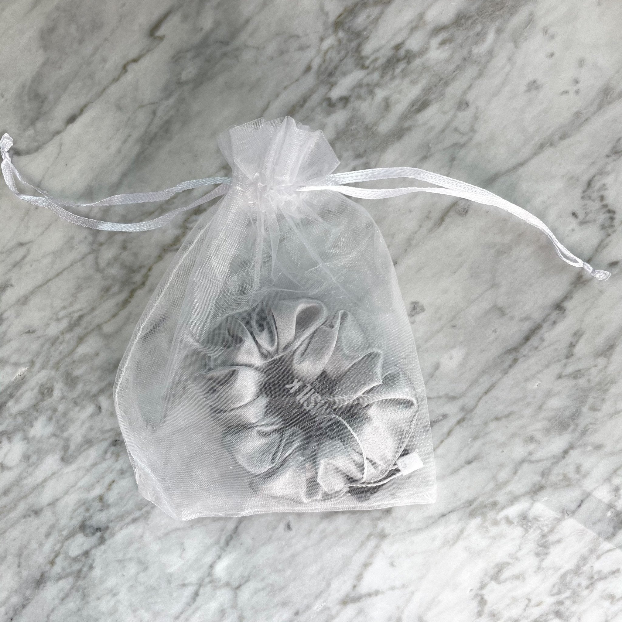 Silver silk scrunchie by DREAMSILK, showing a smooth, shiny fabric hair accessory on a plain background.