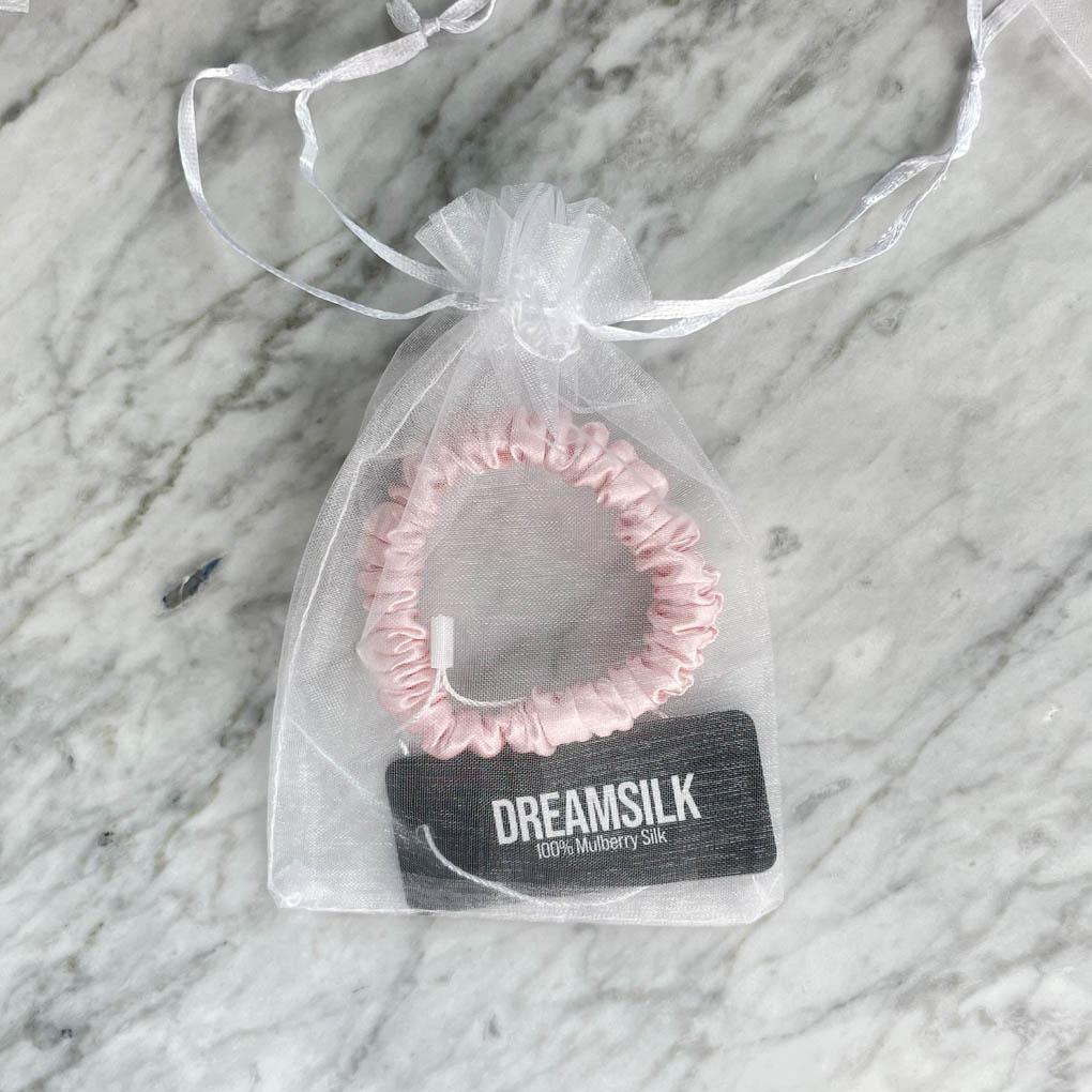 Pink silk scrunchie from DREAMSILK with a skinny design, shown wrapped around a section of hair.