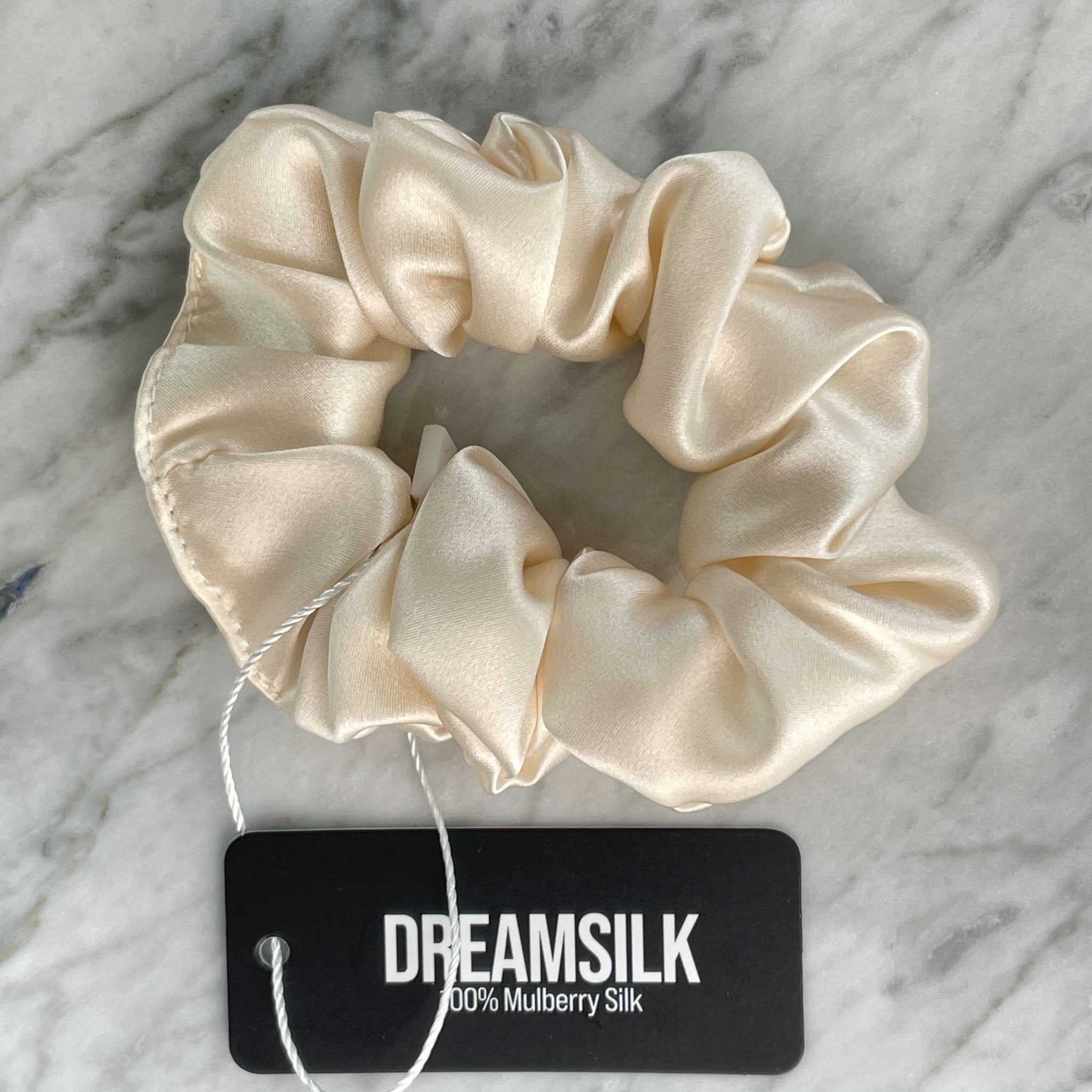 Champagne-colored silk scrunchie by DREAMSILK with a smooth, shiny finish, shown on a white background.