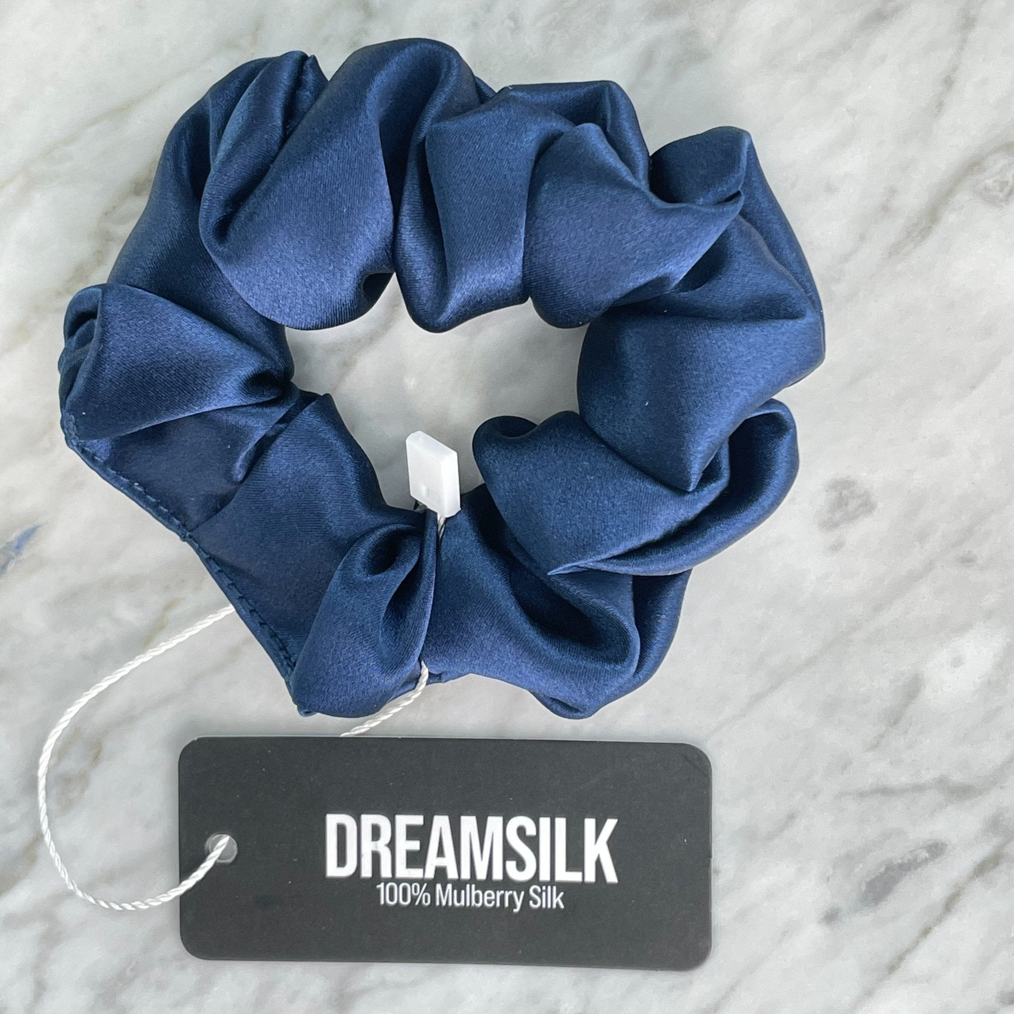 Navy blue silk scrunchie by DREAMSILK, shown on a white background, highlighting its smooth, shiny silk fabric and elastic band.