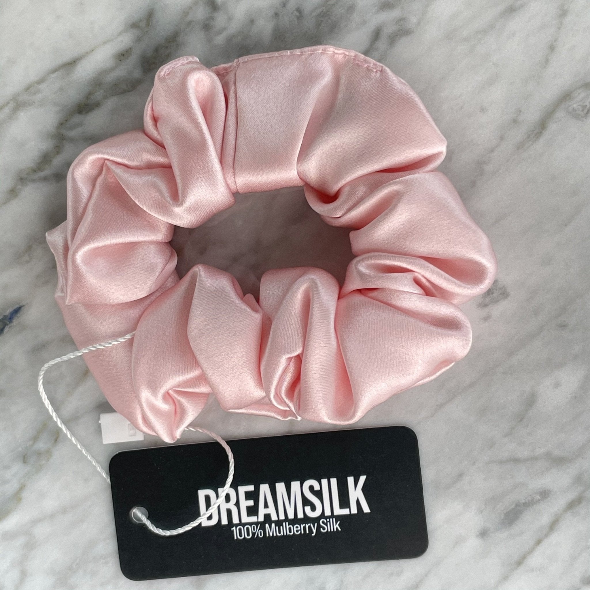 Pink silk scrunchie from DREAMSILK, regular size, soft and shiny fabric, shown wrapped around a hair strand.