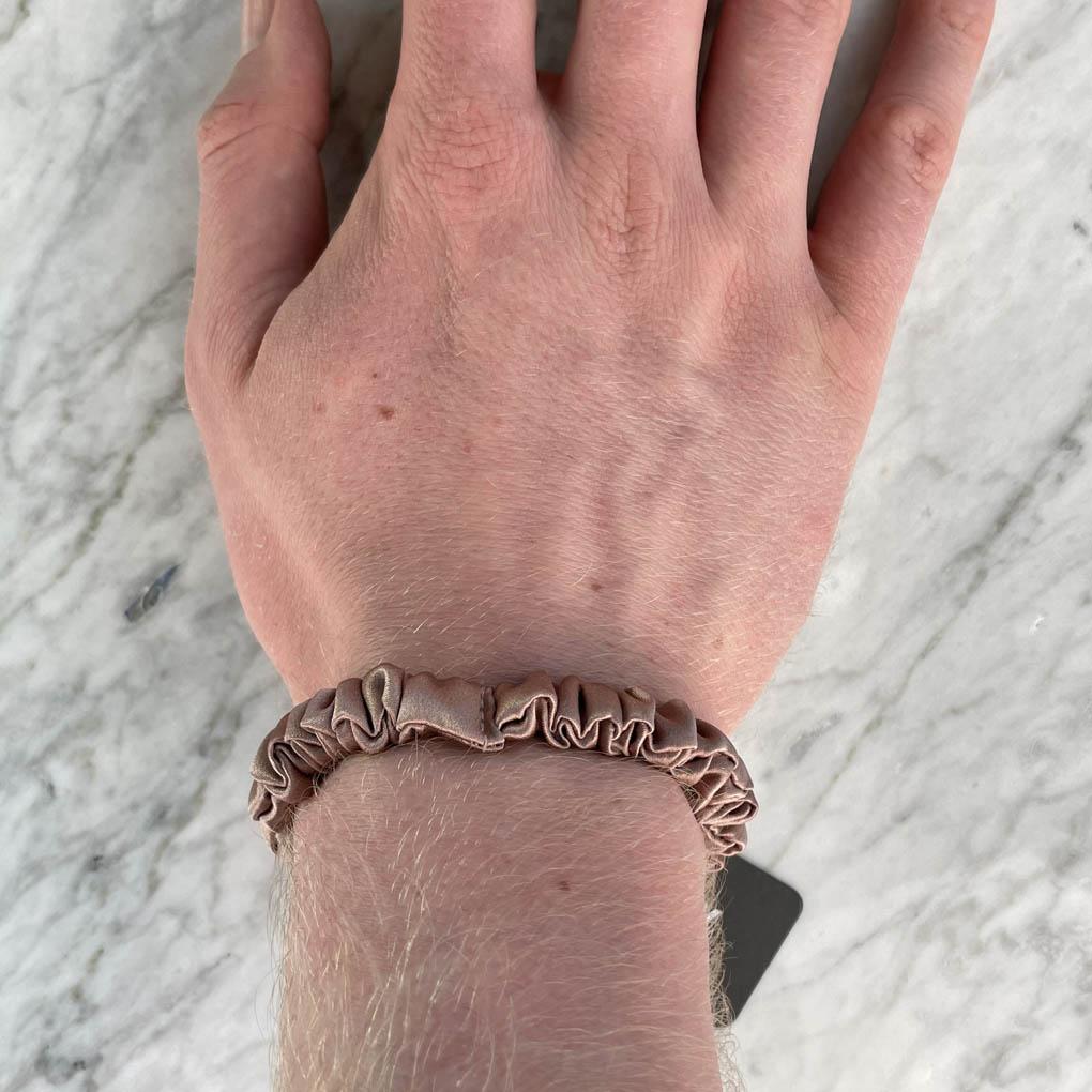 Bronze silk scrunchie from DREAMSILK, a skinny hair accessory made of smooth, shiny silk fabric, shown coiled on a white background.