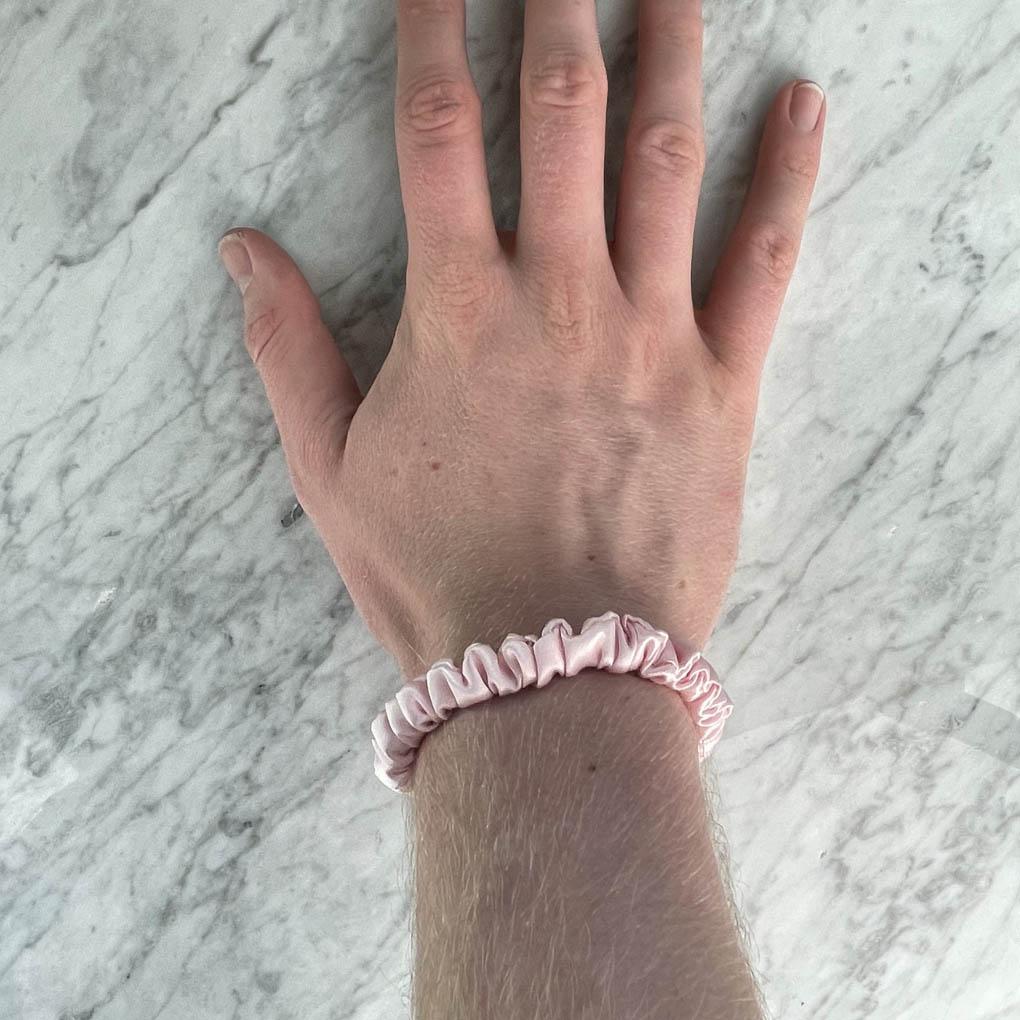 Pink silk skinny scrunchie from DREAMSILK, showing its smooth, shiny fabric and slim design on a neutral background.