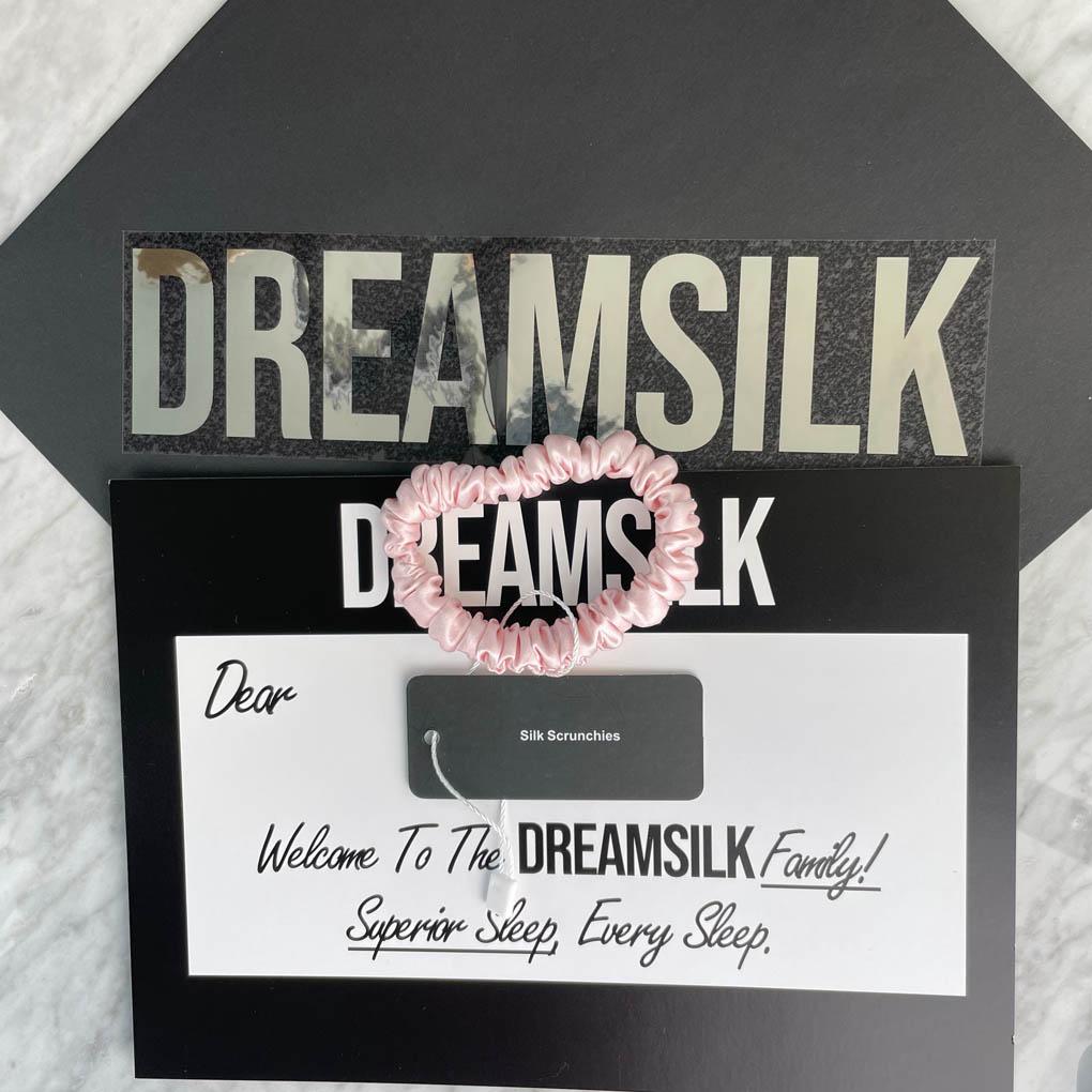 Pink silk scrunchie by DREAMSILK, skinny style, shown wrapped around a section of smooth hair for a soft, elegant look.