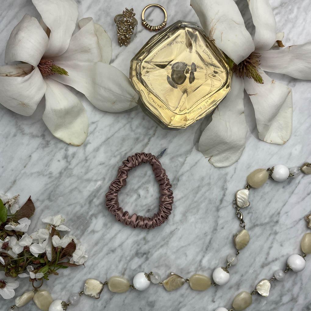 Bronze silk scrunchie by DREAMSILK, slim and lightweight, shown on a soft fabric background.