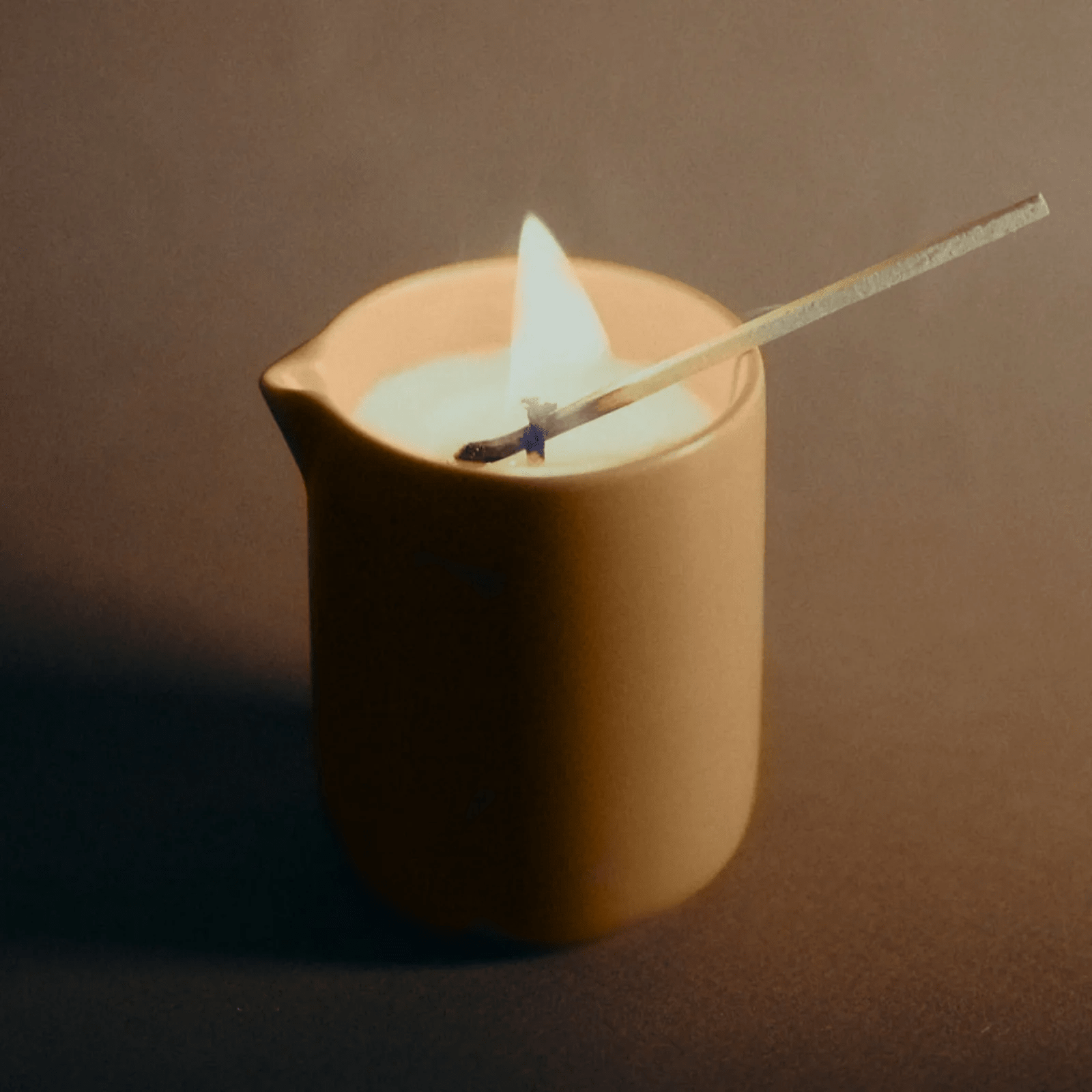 Scented massage candle by Musketeers with mandarin and sandalwood scent, showing a lit candle and soft pillows.
