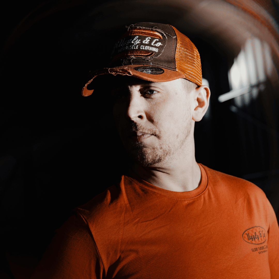 Rust Uggly and Co flat track trucker cap with mesh back and curved brim, featuring a rugged, vintage-inspired design.