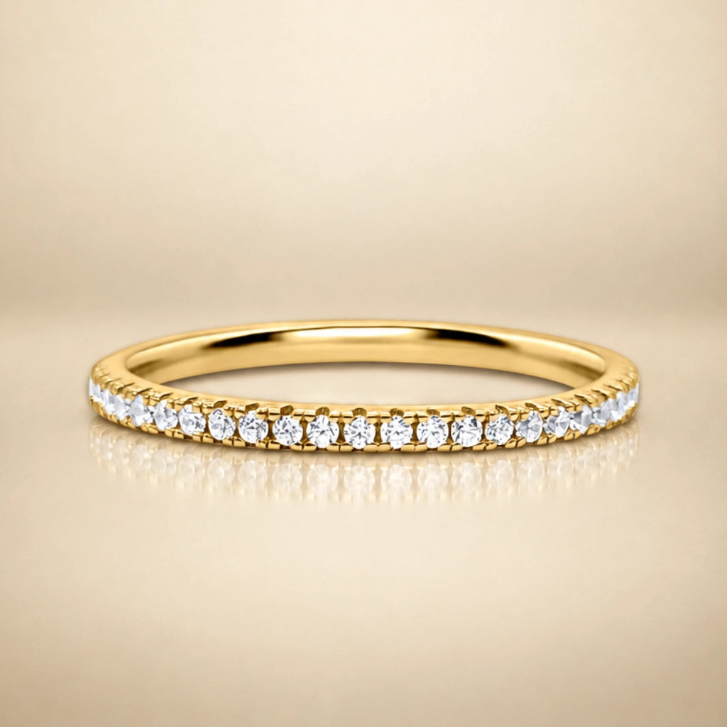A yellow gold eternity ring set with a row of round brilliant-cut diamonds on a warm beige background.