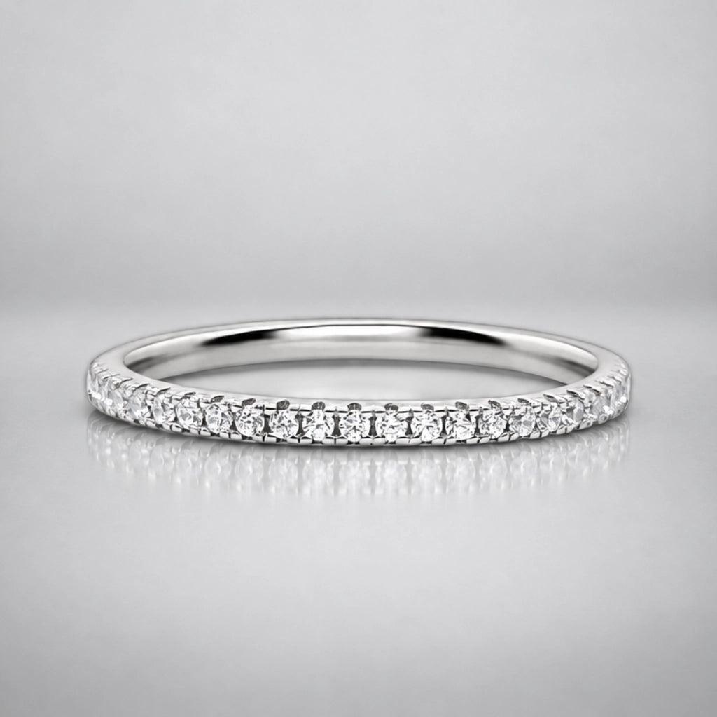 A silver diamond eternity ring with a continuous row of round-cut diamonds set in a polished silver band, shown on a neutral gray reflective surface.