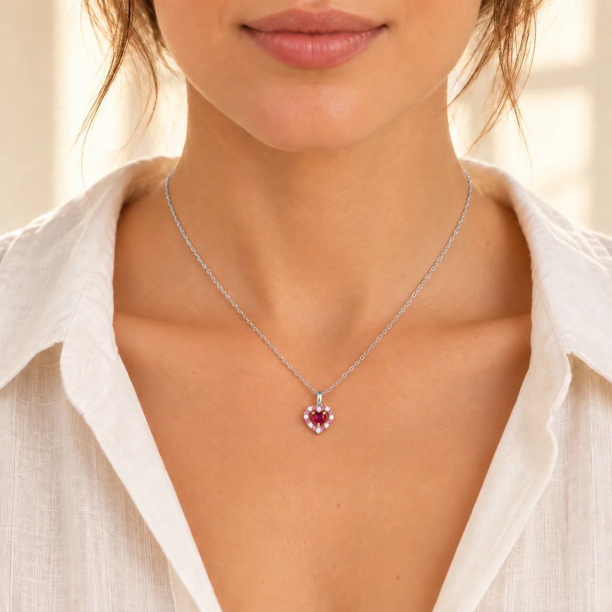 Woman wearing a delicate red heart rhodolite garnet pendant necklace in sterling silver with a cream linen blouse.