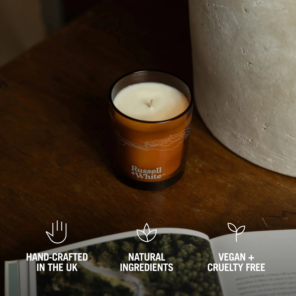 Russell + White Oud Fortune 250g scented soy candle in a glass jar with a lit wick and elegant label.