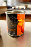 Musketeers Takes Two to Mango mango scented candle with a clear glass jar and orange and yellow wax inside.