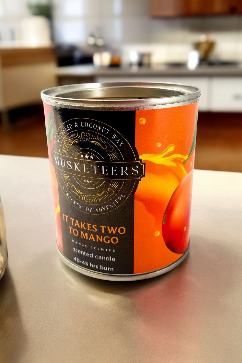 Musketeers Takes Two to Mango mango scented candle with a clear glass jar and orange and yellow wax inside.