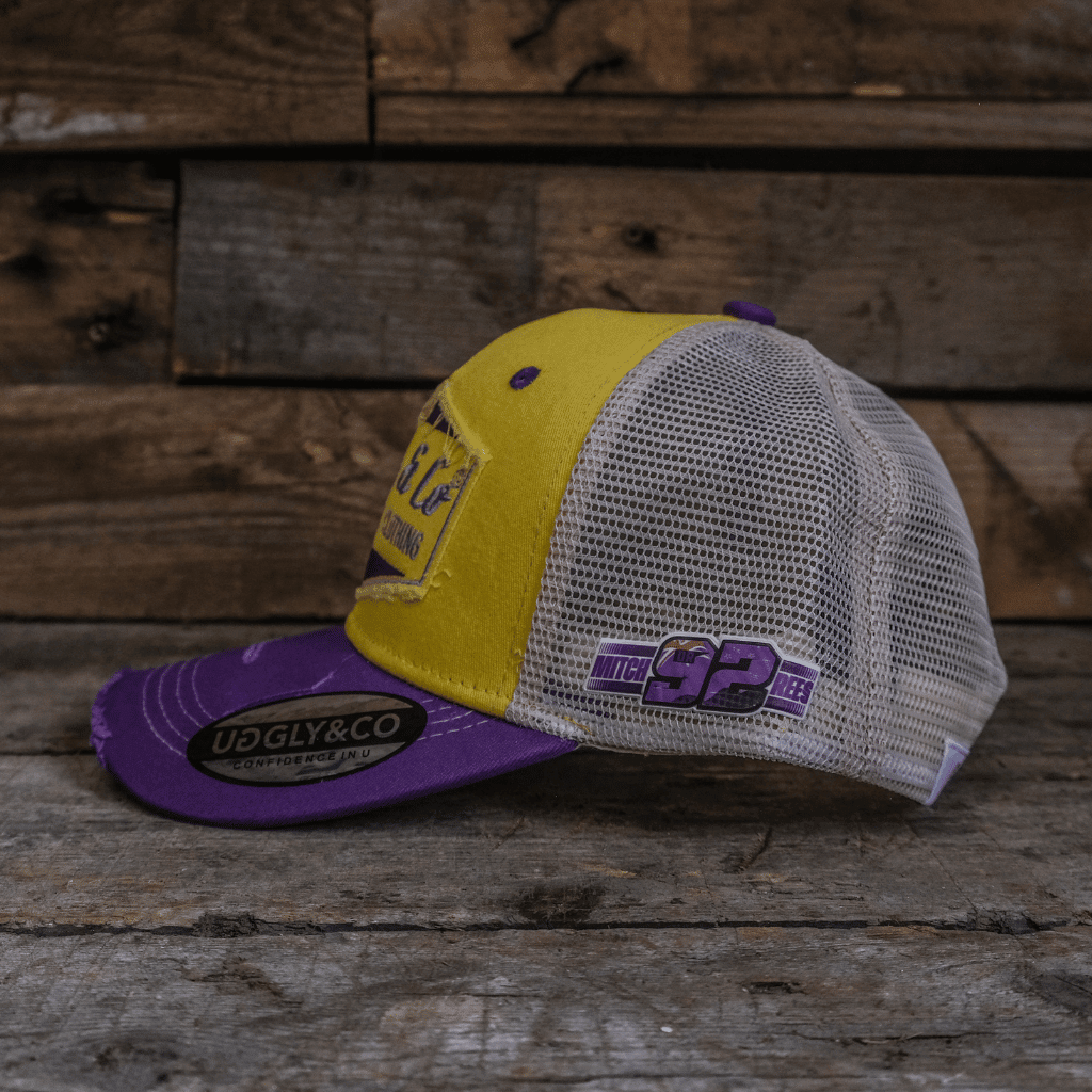 Yellow and purple diamond-patterned Uggly and Co trucker cap with mesh back and adjustable strap.