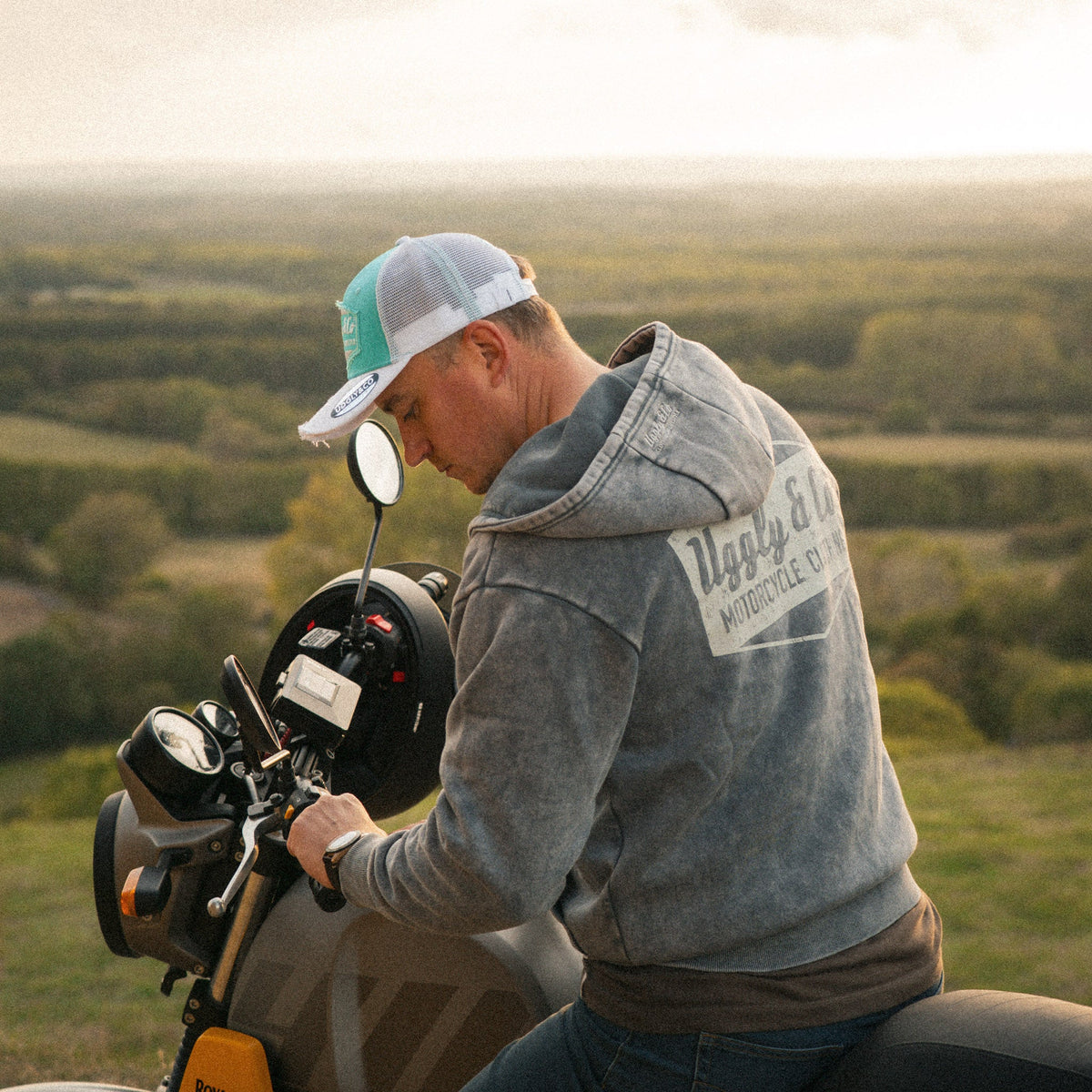 Turquoise and white diamond pattern Uggly and Co trucker cap featuring a motorcycle and Royal Enfield Scram 411 design.