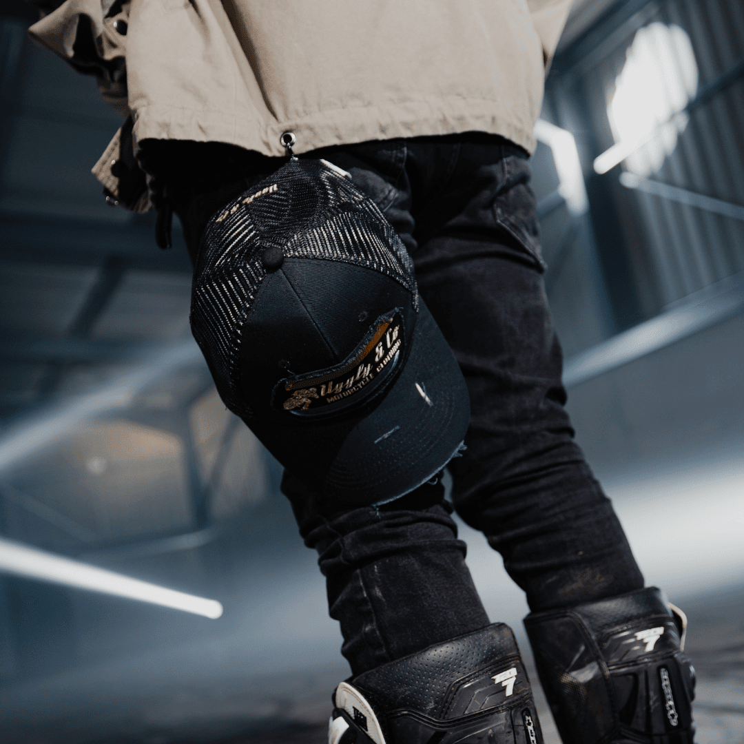 Black flat track trucker cap by Uggly and Co featuring a mesh back and structured front panel with a curved brim.