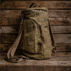 An olive green canvas backpack with military-style stenciled markings, displayed on a rustic wooden plank surface.