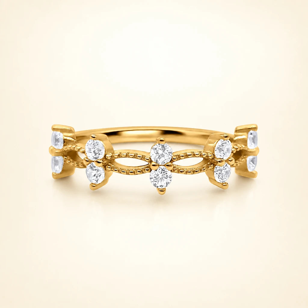 A yellow gold vermeil ring featuring a decorative openwork band with six clear round-cut and square-cut gemstones, set against a soft cream background.
