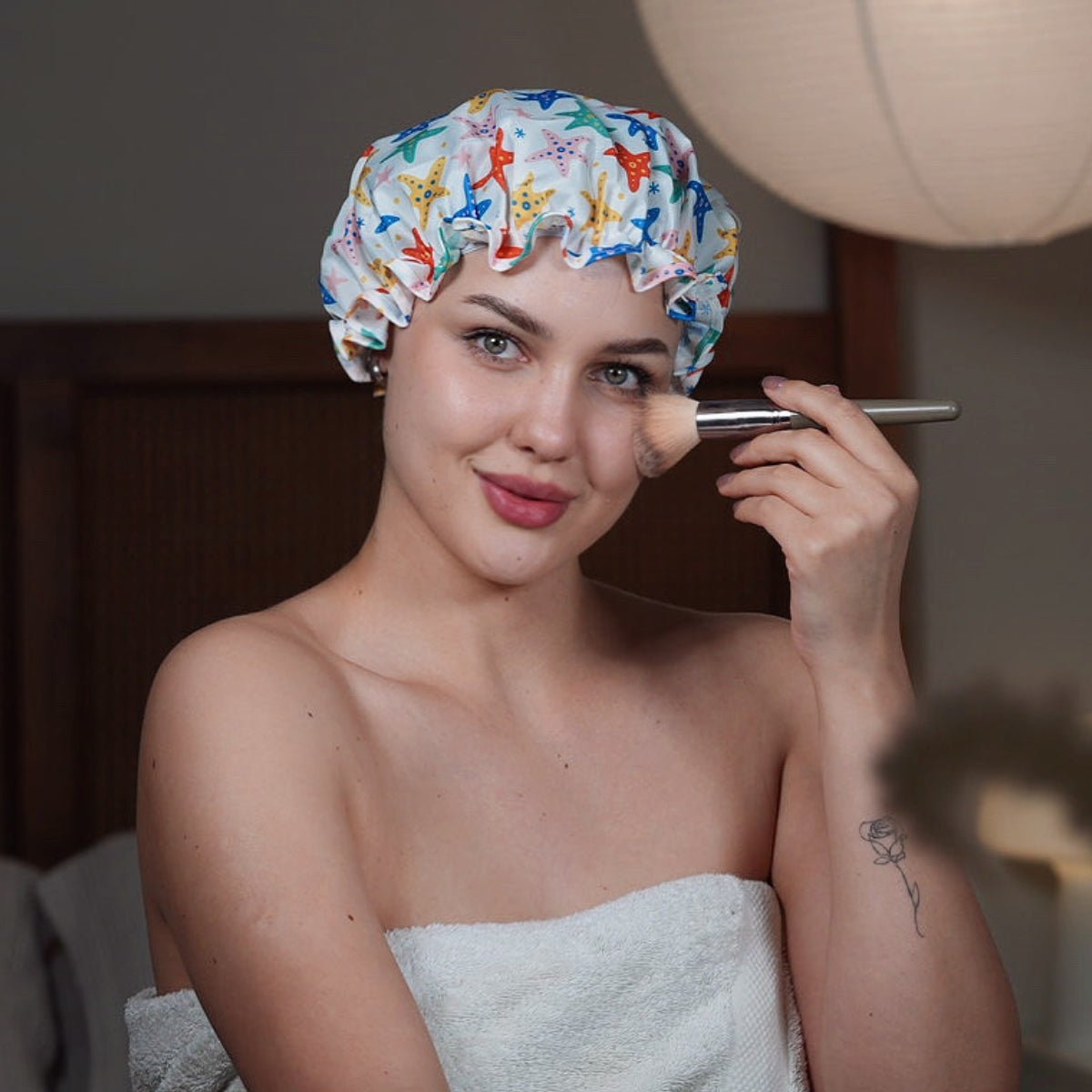 SMUG starfish print shower cap resting on a towel with makeup brushes in the background.