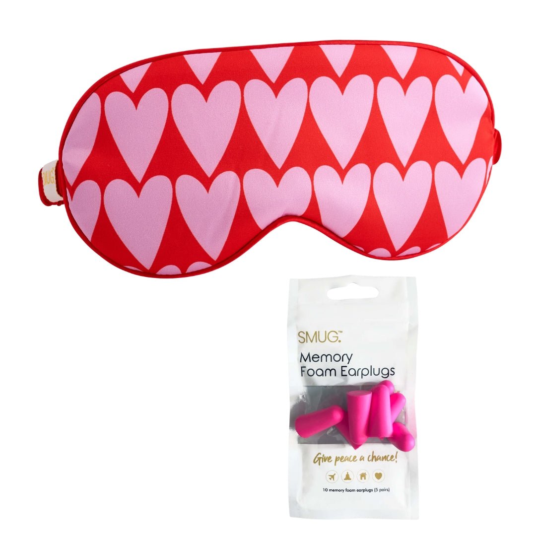 Pink satin sleep mask with longheart print from SMUG, featuring attached earplugs for comfortable, restful sleep.