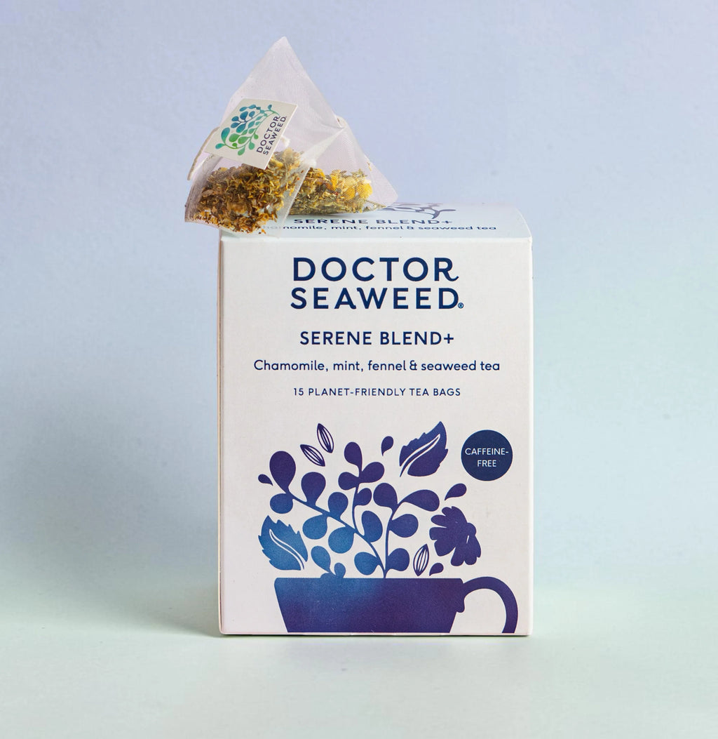 A steaming cup of Serene Blend+ Tea by Doctor Seaweed, with tea leaves and herbs visible on a cozy wooden table.