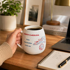 Trouvaille North Carolina map color-in travel mug with a white ceramic surface and a black lid featuring a detailed state outline.