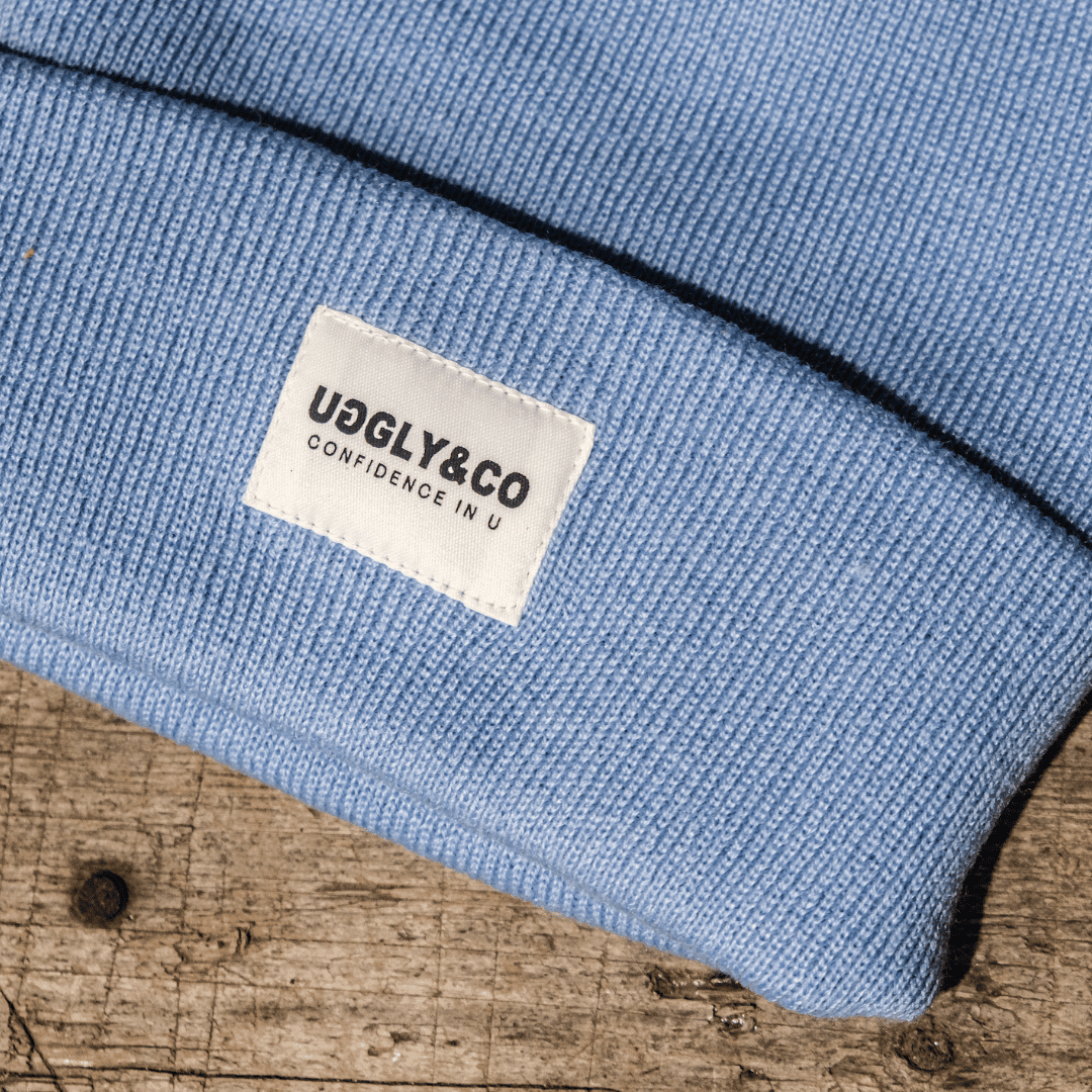 Blue Uggly and Co beanie hat made of soft knit fabric, shown on a plain background with a snug fit and folded brim.