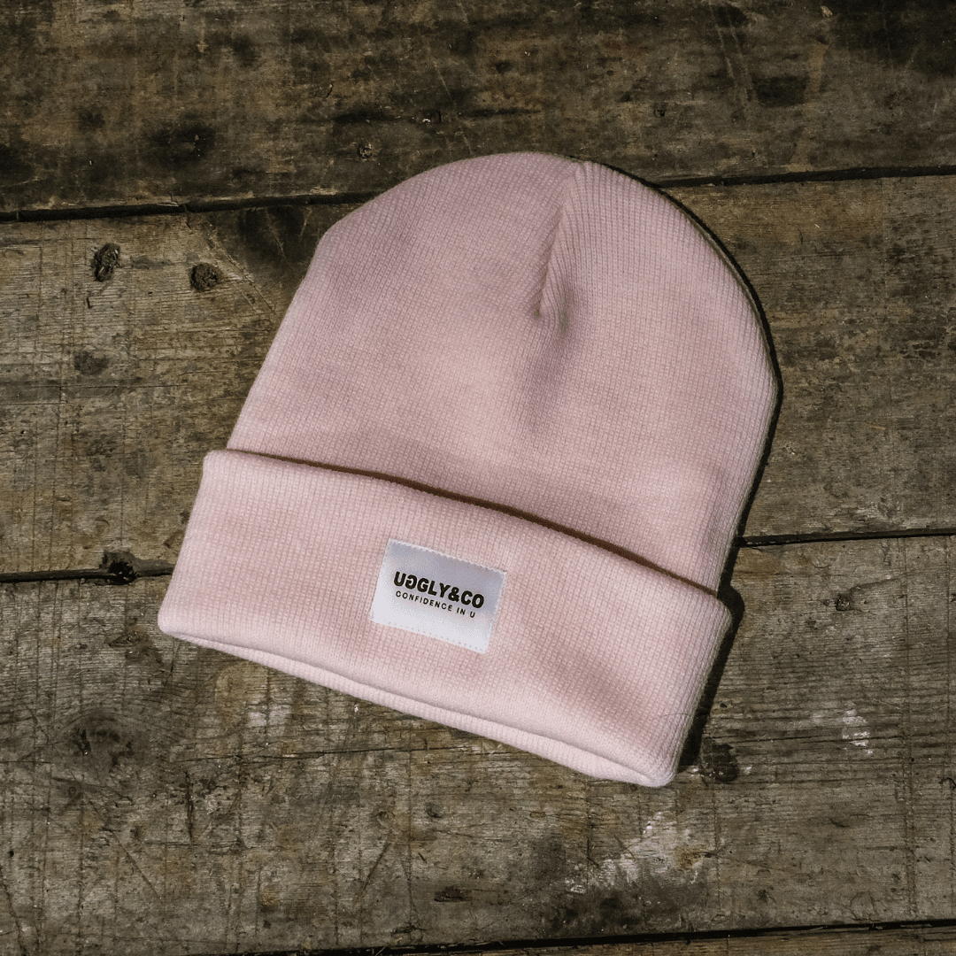 Pastel pink Uggly and Co beanie with a motorcycle knit pattern, soft and cozy for casual winter wear.