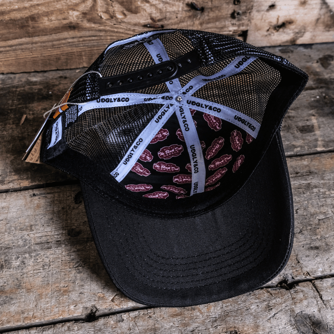Black Dub Garage Trucker Cap by Uggly and Co featuring a classic trucker hat design with mesh back and adjustable snap closure.