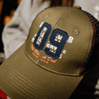 Green Uggly and Co trucker cap with "09" design, featuring mesh back and adjustable strap, casual outdoor headwear.