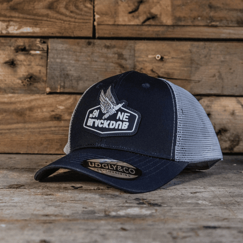Uggly and Co Mile 9 Wings trucker hat with mesh back and embroidered wing design in black and white.