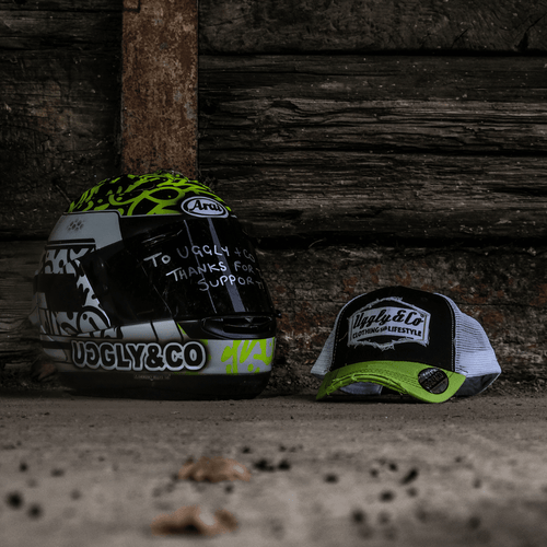 Yellow and white diamond-patterned Uggly and Co trucker cap with mesh back and adjustable strap.