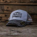 Grey and white diamond-patterned Uggly and Co trucker cap featuring mesh sides and adjustable strap.