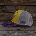 Yellow and purple diamond-patterned Uggly and Co trucker cap with a classic structured design and adjustable strap.