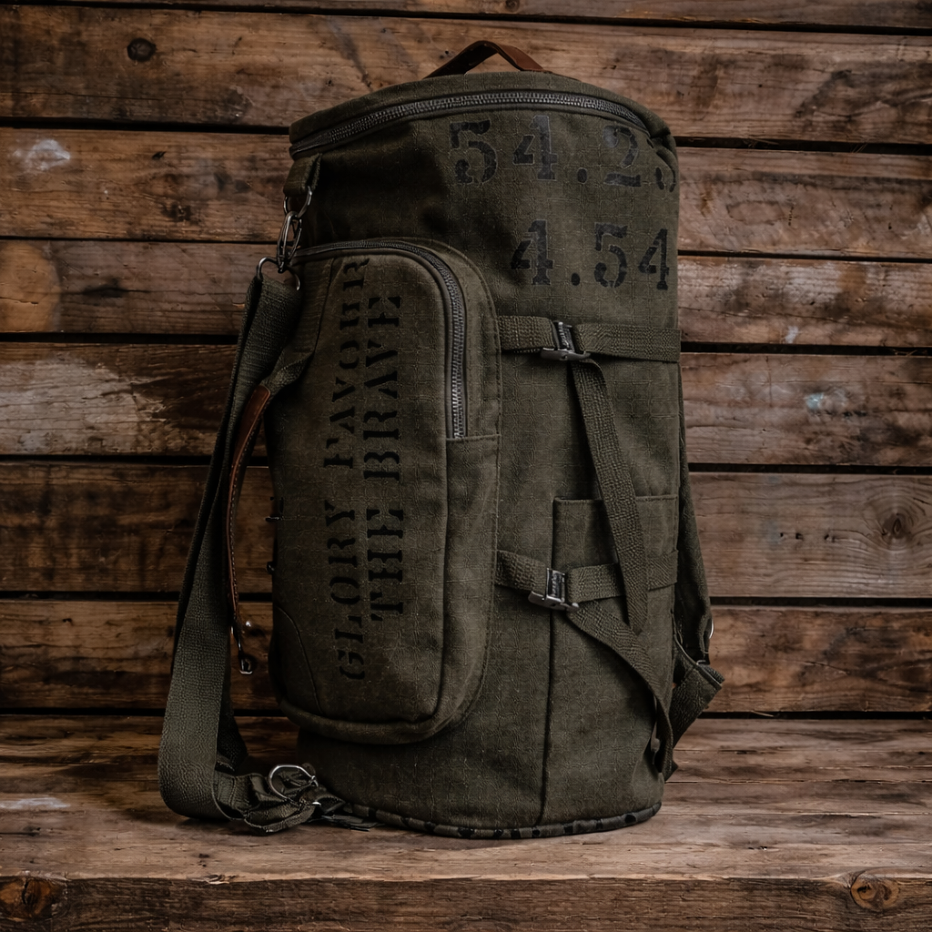 An olive green canvas military-style backpack with distressed black stenciled text and numbers, standing on a wooden surface against a wooden plank background.